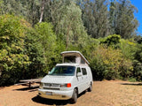 Pop-top VW camper van RV rental set up at a scenic, sunny campsite with a picnic table.