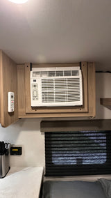 RV rental interior: window AC unit, solar outlet, and countertop. Compact and equipped for comfortable travel.