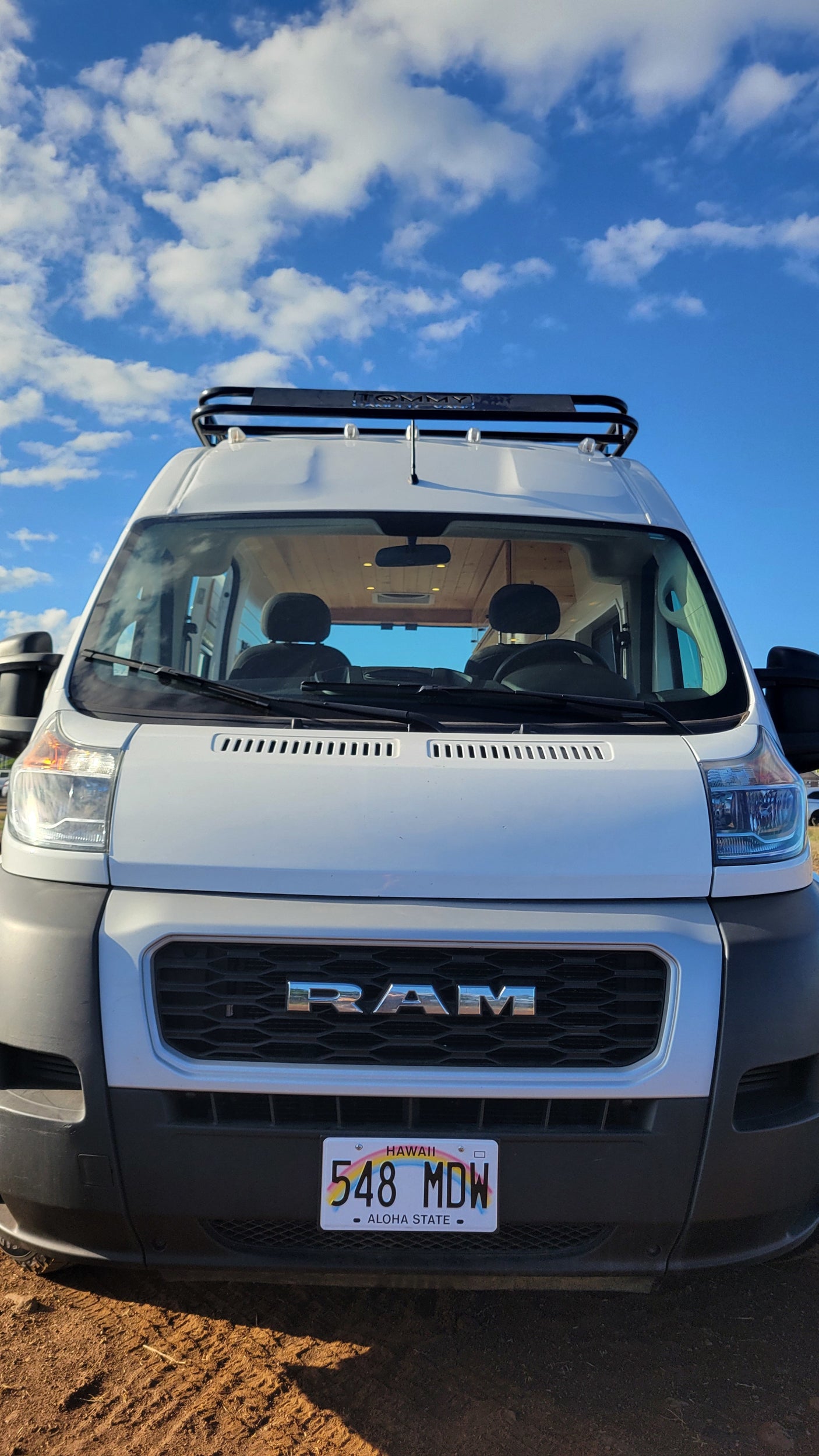 Front view of a white Ram ProMaster RV rental from Hawaii with a roof rack against a blue sky.