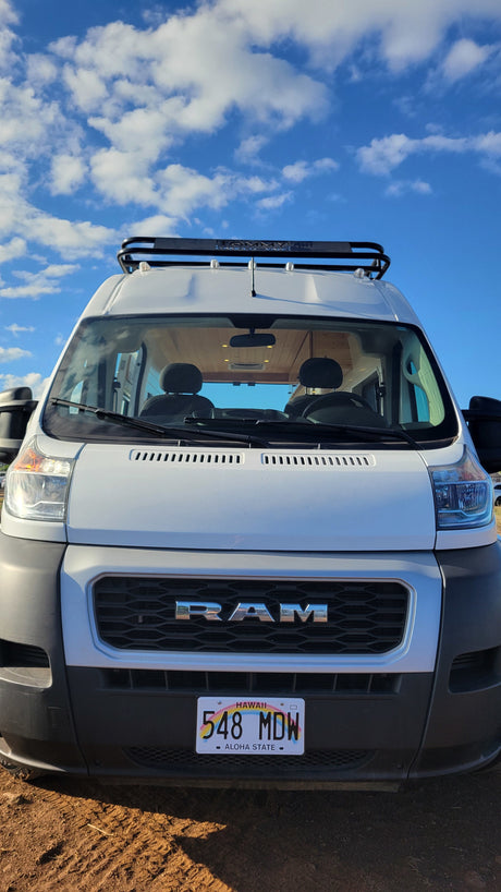 Front view of a white Ram ProMaster RV rental from Hawaii with a roof rack against a blue sky.