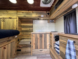 Rustic RV rental interior featuring warm wood paneling, white subway tile kitchen, comfortable bed, and clever storage.