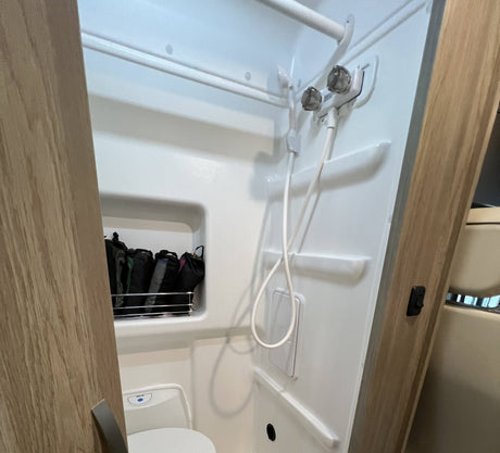 This RV rental features a compact bathroom with a shower, toilet, and built-in storage, ideal for travel comfort.
