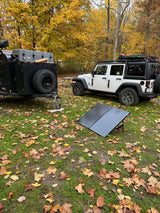 White Jeep & overland RV rental trailer setup with portable solar panels at an autumn campsite amidst golden leaves.