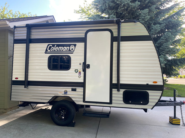 Side view of a white and black Coleman travel trailer, an ideal RV rental.