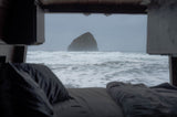 Cozy RV rental view of a majestic sea stack & crashing ocean waves, seen from a comfortable bed inside.