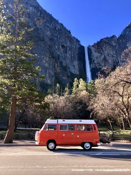 An orange RV rental van parked below the towering Yosemite Falls. Explore stunning national parks like this!