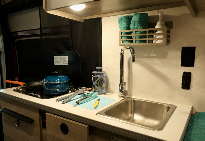  parked by a snowy road in a winter forest.|This RV rental features a functional camper van interior with a kitchen sink — photo 9