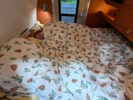 Person sleeping peacefully in a cozy RV rental bed with festive pinecone duvet, ideal for comfortable travel.