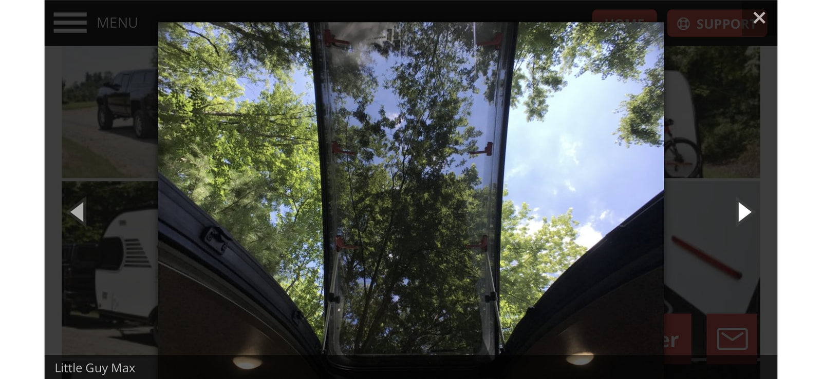 Inside an RV rental: Looking up through a skylight at bright blue sky and lush green tree canopies.