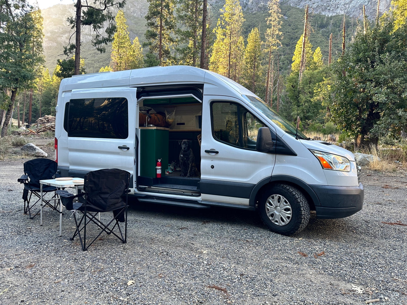  with a person cooking outdoors next to it. Tall trees and rocks line the road.|RV rental interior: overhead kitchen cabinet with dishes — photo 13