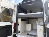 This inviting RV rental interior features an elevated bed, pull-out storage, and outdoor shower hookup, ready for adventure.