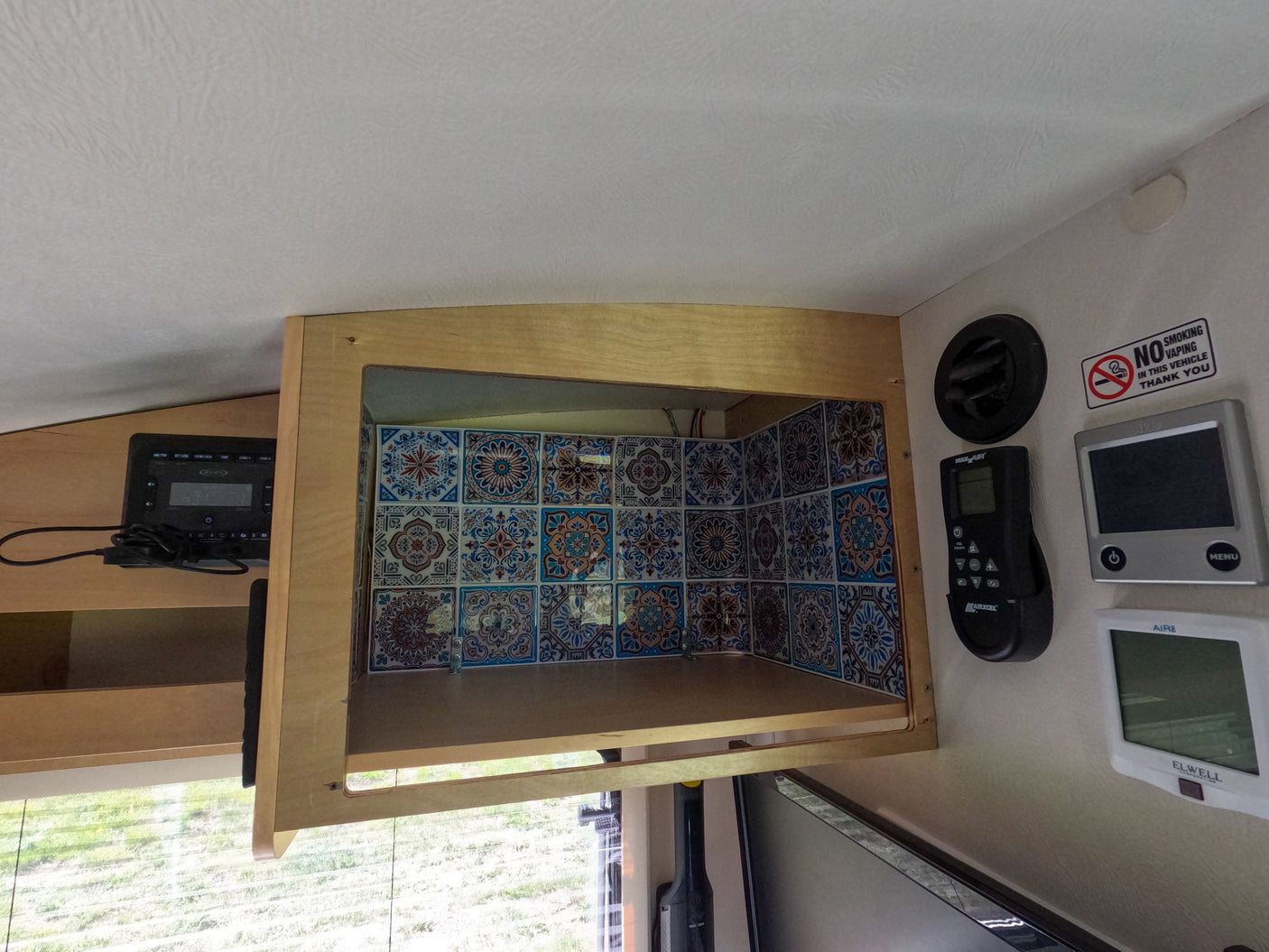 RV rental interior: open tiled overhead cabinet, power monitor, and various wall controls for fan and climate.
