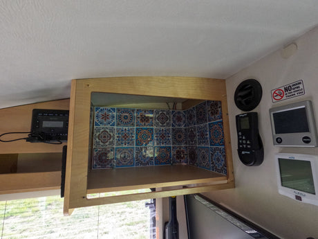 RV rental interior: open tiled overhead cabinet, power monitor, and various wall controls for fan and climate.