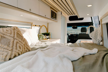 Modern RV rental interior with a cozy bed, compact kitchen, and overhead storage. Enjoy scenic views while traveling.