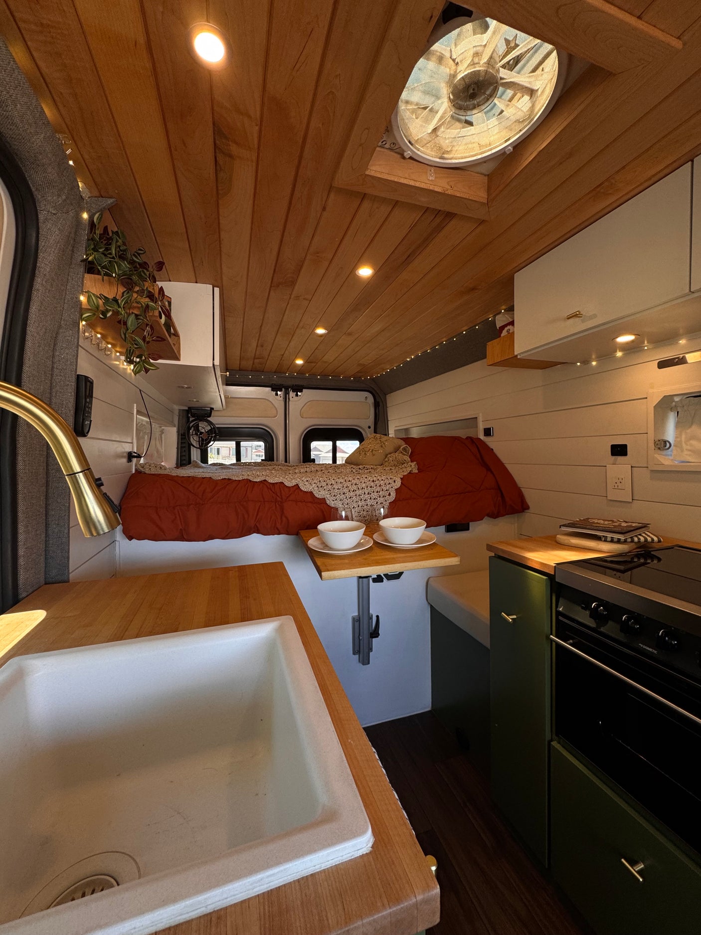 Cozy rv rental interior: wooden ceiling, built-in bed, and kitchen with sink & stove, ready for adventure.