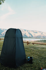 RV rental adventure: Black privacy tent & grill on green grass near a lake, framed by distant mountains.