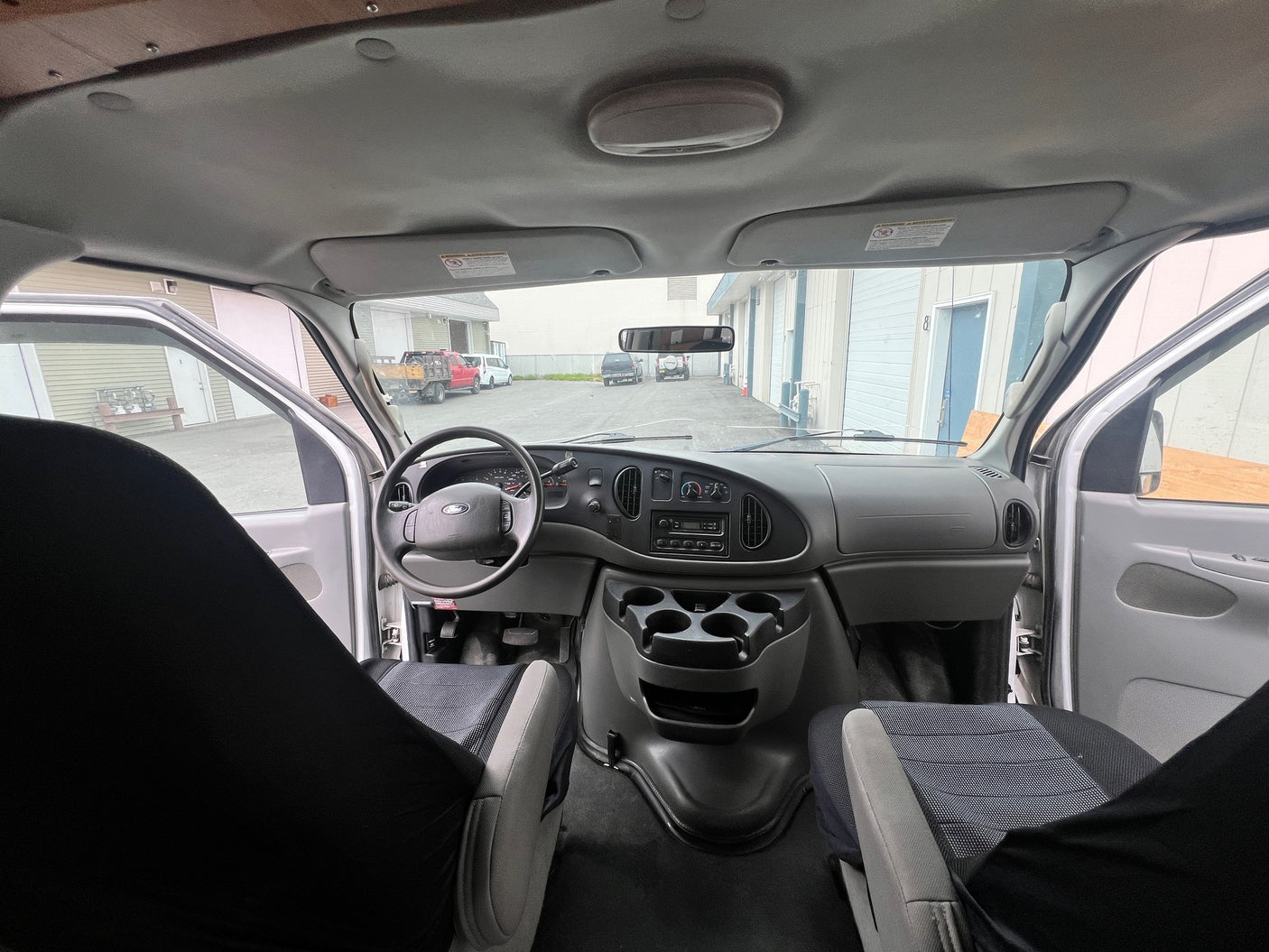 Interior of a Ford **RV rental** van, looking forward. Features include the dashboard, steering wheel, front seats, and the exterior through the windshield.