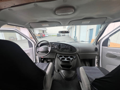 Interior of a Ford **RV rental** van, looking forward. Features include the dashboard, steering wheel, front seats, and the exterior through the windshield.