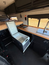 Inside this modern rv rental, a compact camper van features a pull-out fridge, sink, stovetop, and bed.