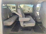 RV rental vehicle's grey interior with passenger seating. Large RVs are visible parked outside through the windows.
