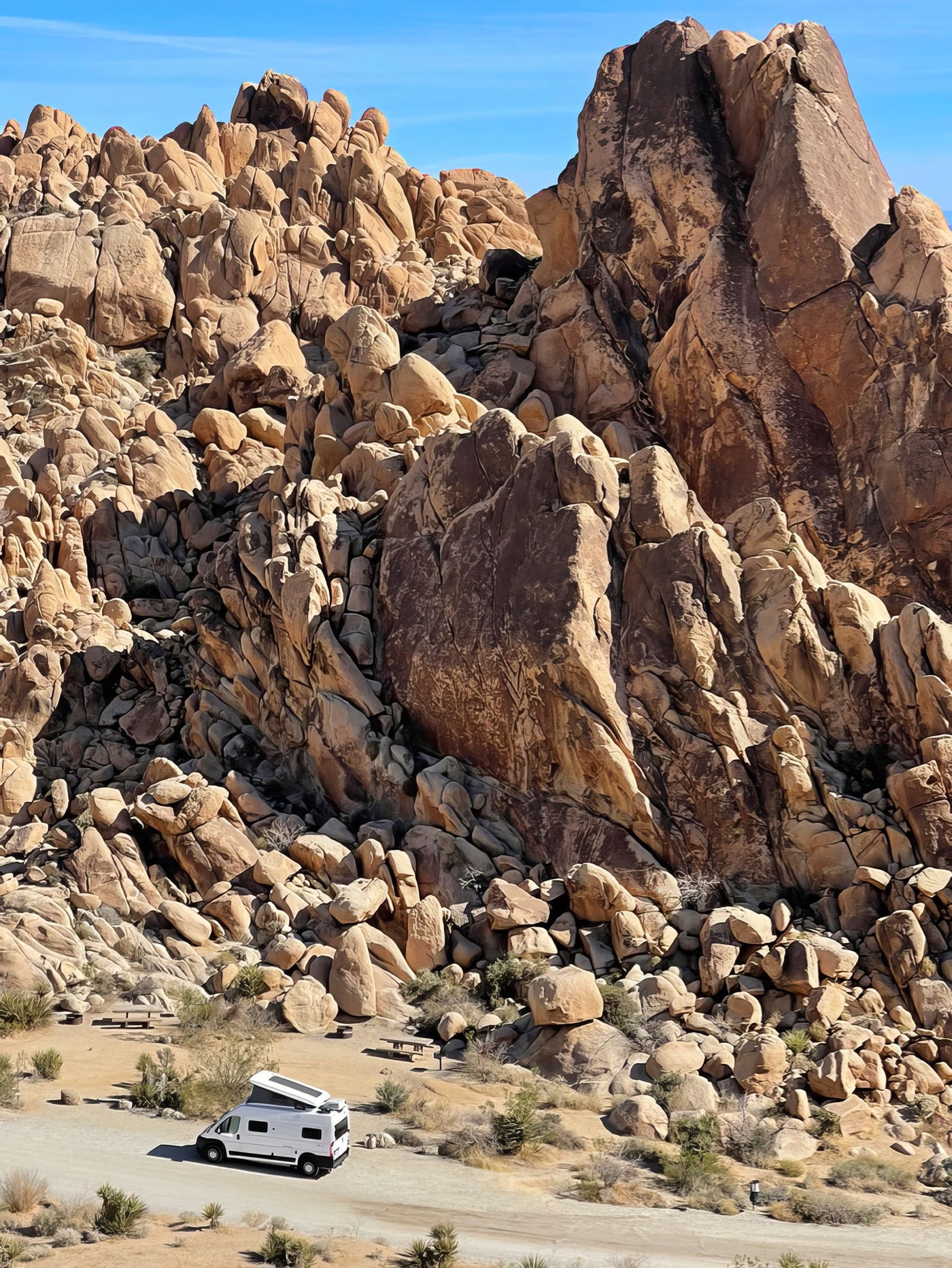 White RV rental parked in a rugged desert landscape among massive rock formations under a clear blue sky. — photo 6