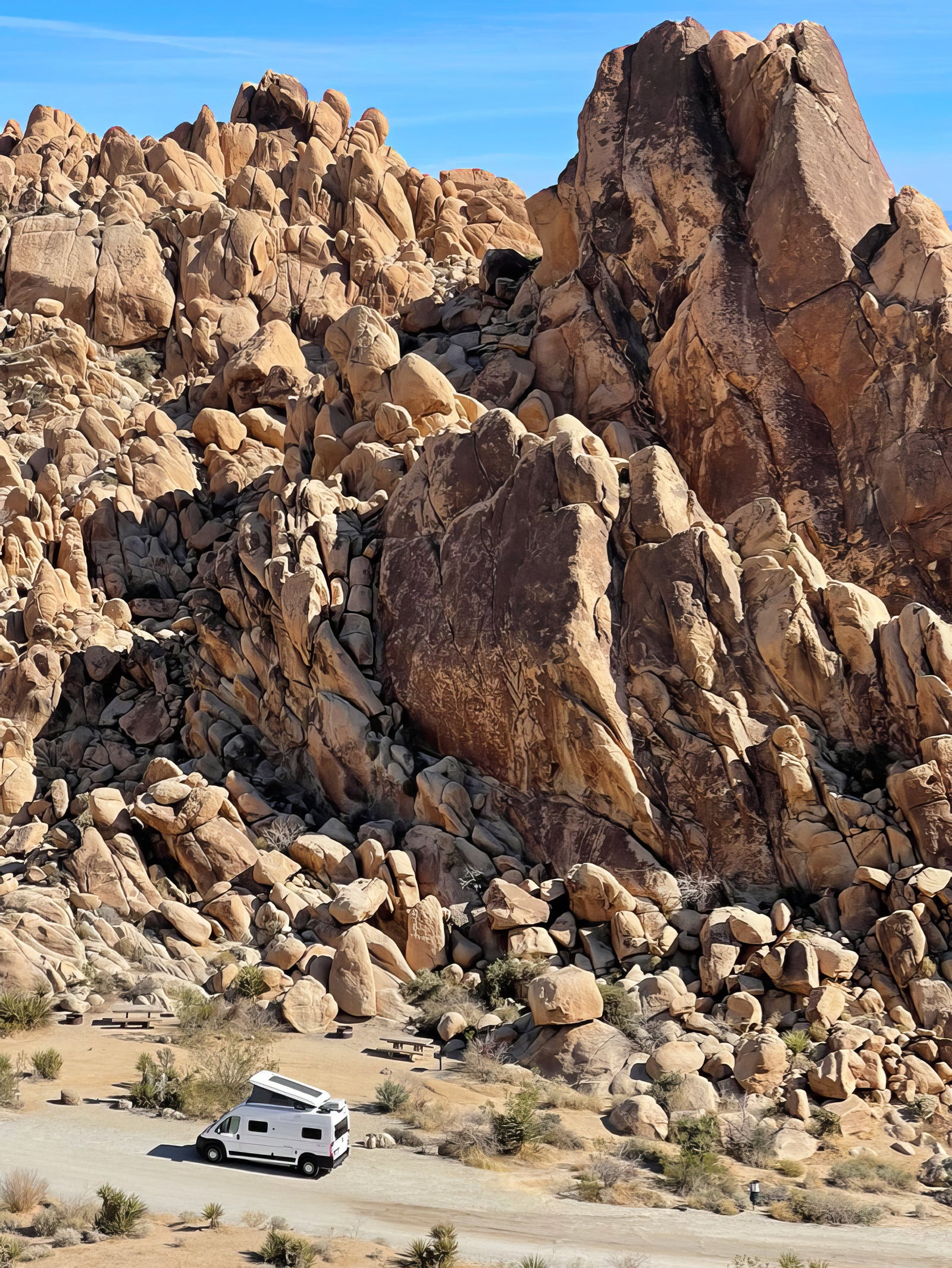 White RV rental parked in a rugged desert landscape among massive rock formations under a clear blue sky.
