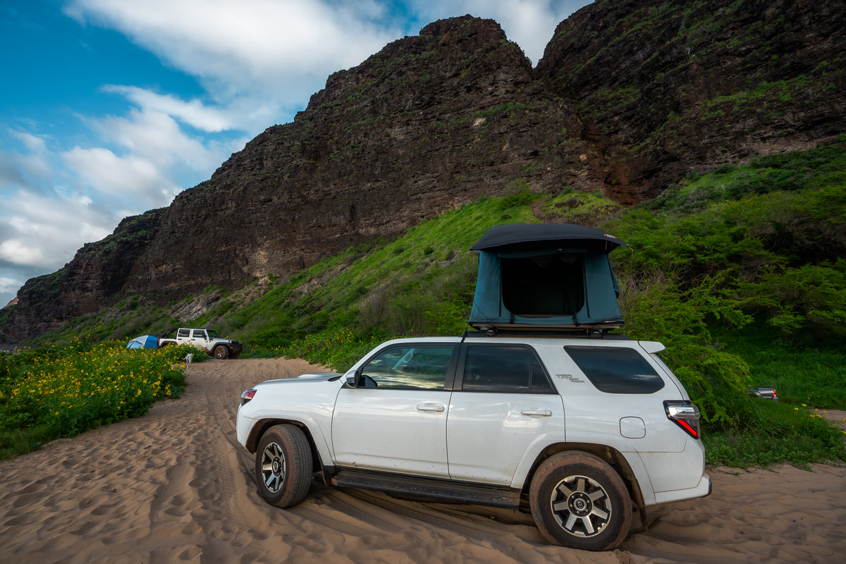 White RV rental SUV with rooftop tent on a sandy path near towering cliffs & lush greenery, ideal for off-road camping. — photo 12