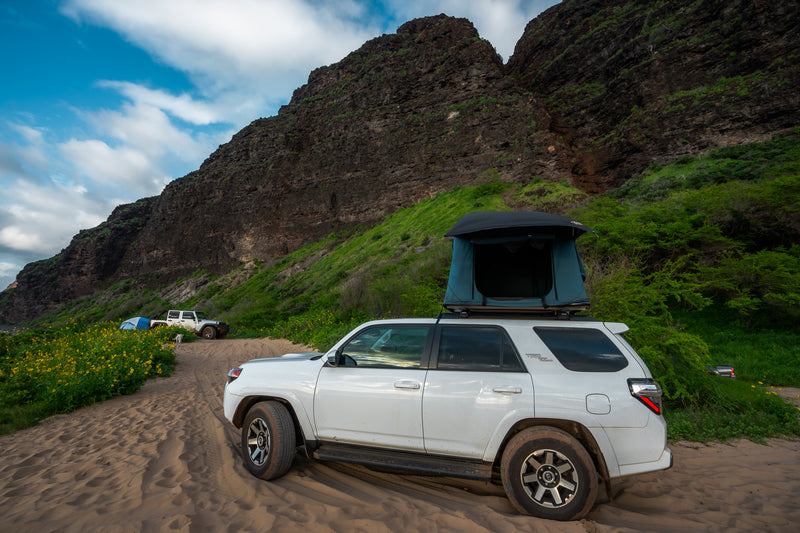 White RV rental SUV with rooftop tent on a sandy path near towering cliffs & lush greenery, ideal for off-road camping. — photo 12
