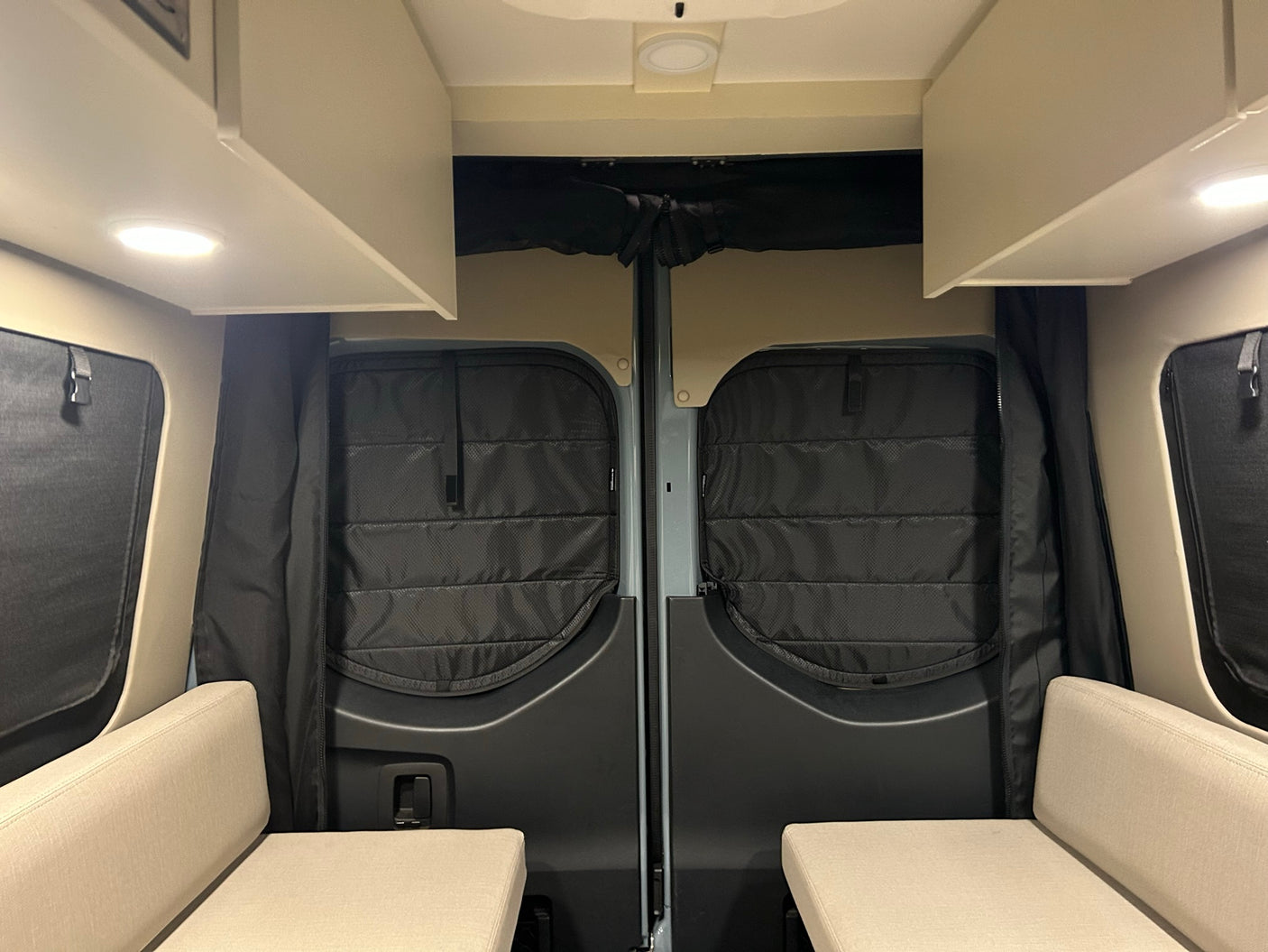 Cozy rv rental interior looking towards the rear doors. Features include quilted insulation, overhead cabinets, and two bench seats.