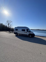 RV rental van parked on asphalt by a serene lake under a bright blue sky, perfect for a sunny getaway.