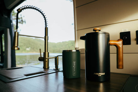 RV rental interior featuring a stylish kitchen with a brass faucet, coffee essentials (French press, travel mug), and a lake view.