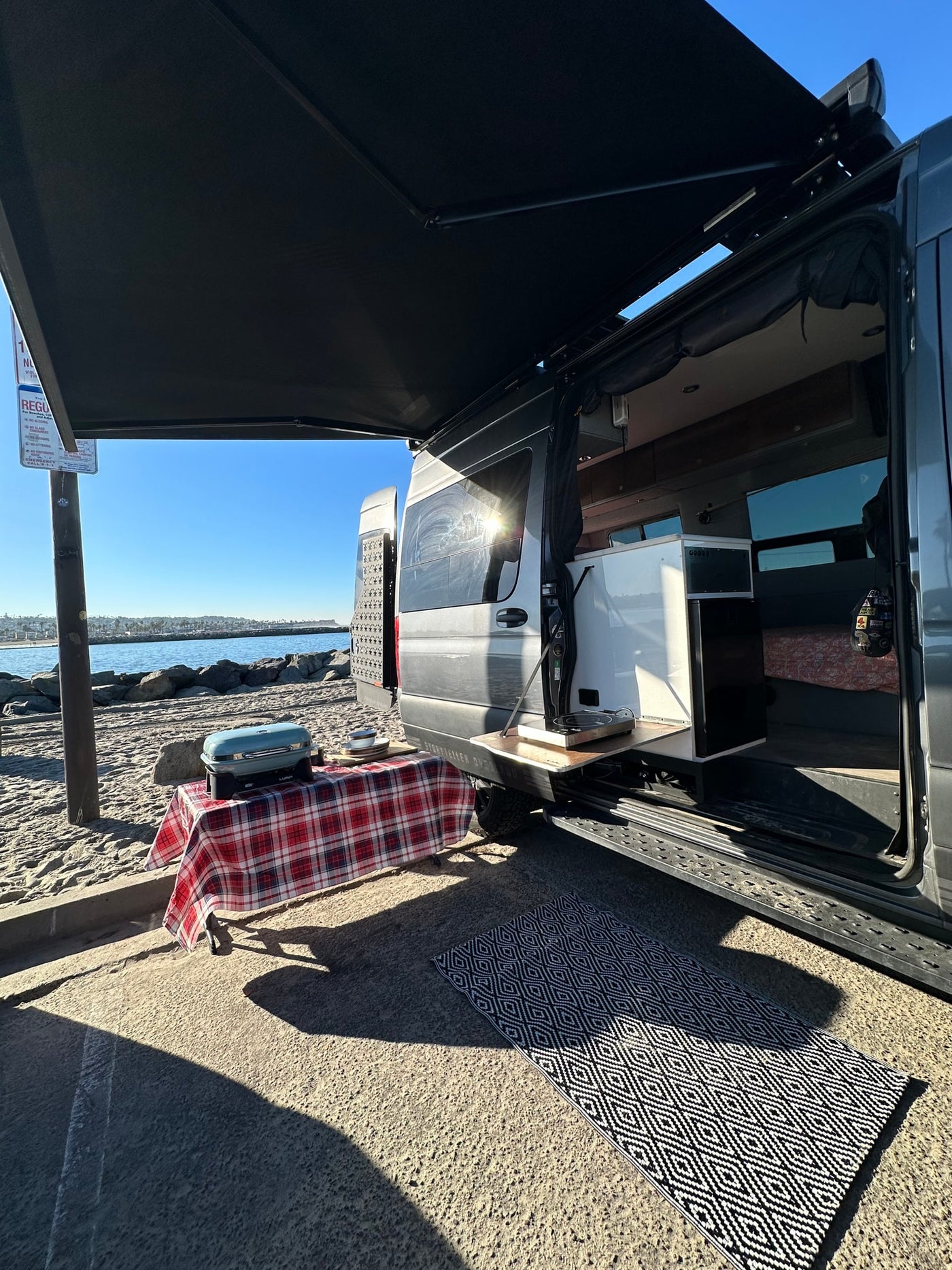An RV rental parked on a sandy shore, ready for outdoor cooking with its awning extended and door open. — photo 10