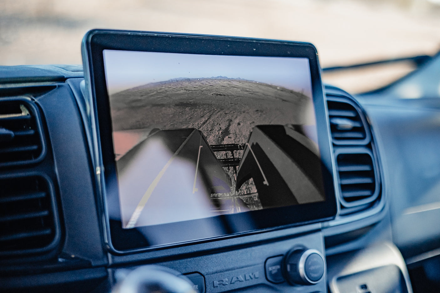 Inside an RV rental, the central screen displays a wide-angle backup camera view of the rear and distant landscape, surrounded by air vents.