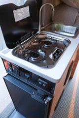 Compact RV rental kitchen: two-burner stove, sink, faucet, and Nova Kool fridge for convenient cooking on the go.