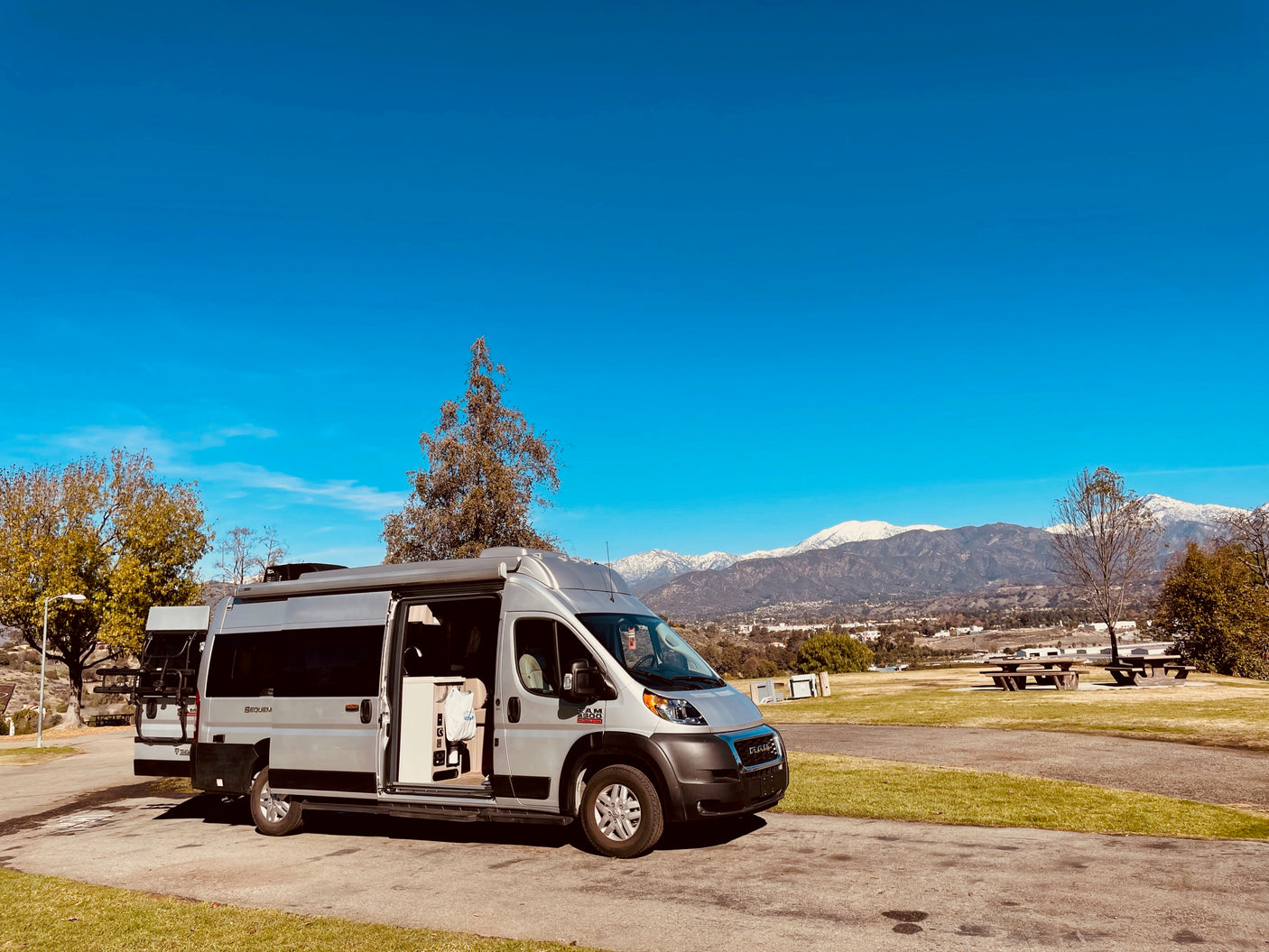 An RV rental camper van with open doors, showing its interior, parked in a scenic spot overlooking snow-capped mountains.