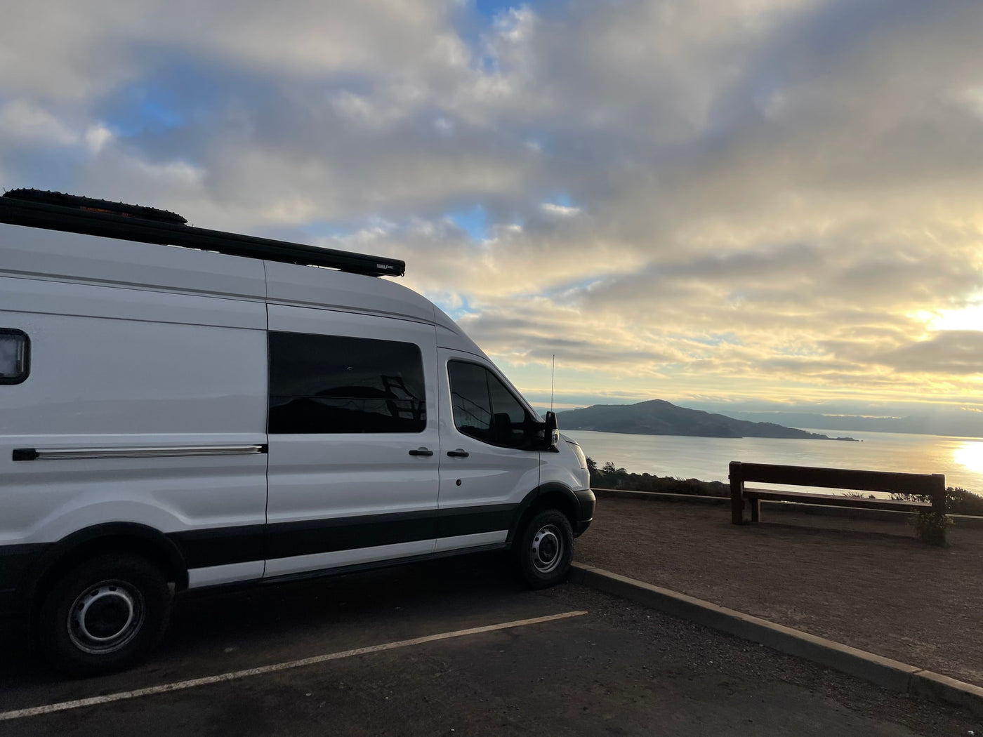 White RV rental van parked overlooking a serene bay with hills at sunset, ideal for scenic travel. — photo 2