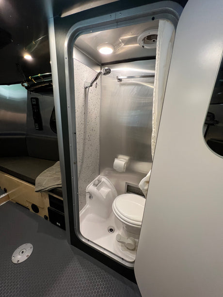 Efficient RV rental wet bath with toilet, shower, and integrated sink in a modern, metallic interior.