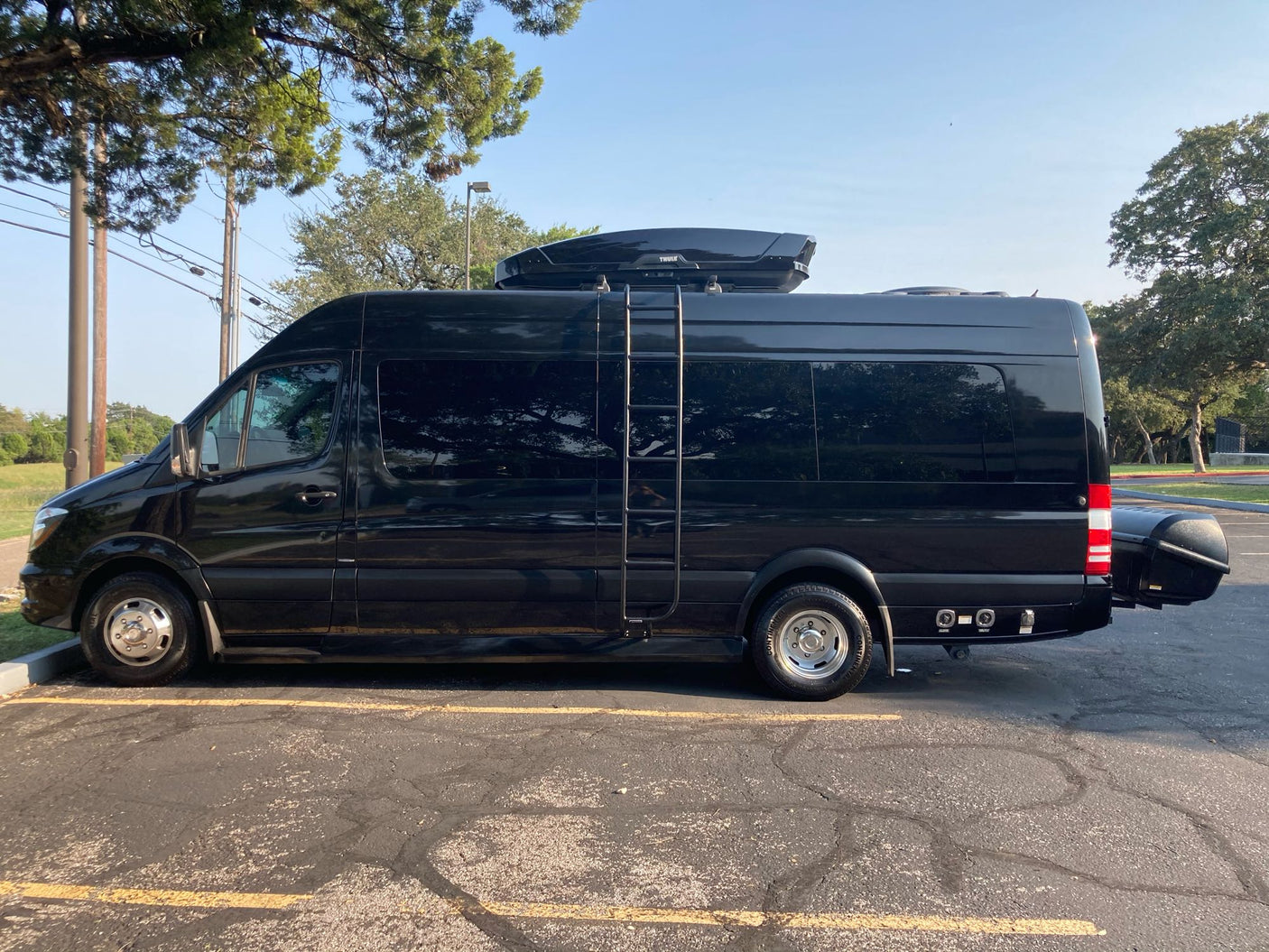 Black Mercedes Sprinter van RV rental, equipped with roof box, side ladder, and rear cargo for your next adventure.