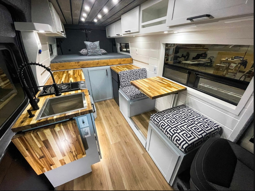 Explore this modern RV rental interior featuring a full kitchen with wood counters, comfortable dining area, and cozy bed.