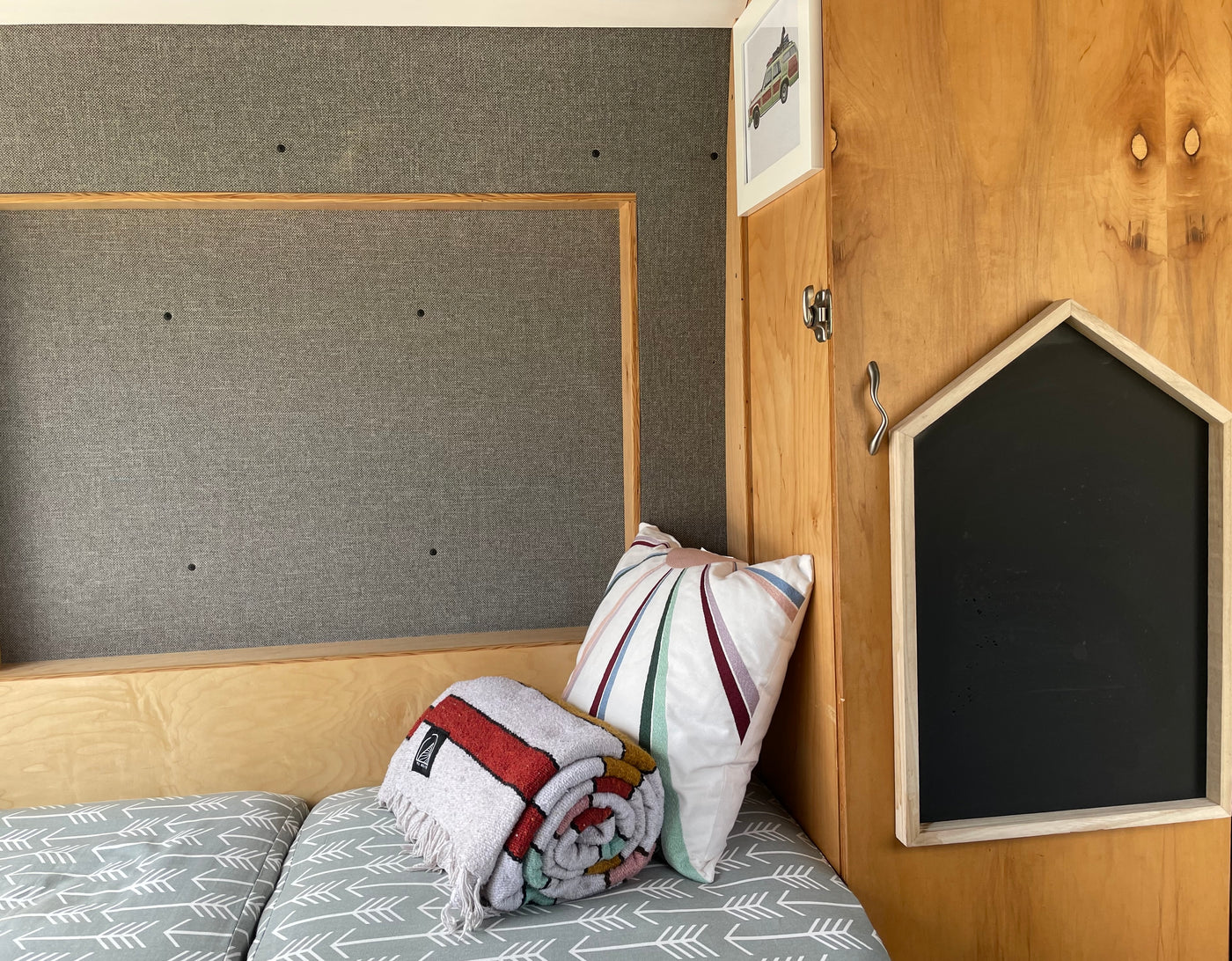 Cozy RV rental interior with bed, colorful blanket, striped pillow, wood panels, and a house chalkboard. — photo 13