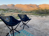 Relaxing at our RV rental desert campsite. Two chairs face golden mountains and open skies, perfect for outdoor travel.