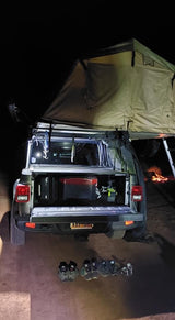 Nighttime overlanding setup: Jeep Gladiator with rooftop tent deployed. Gear in truck bed, shoes on ground. Great for RV rental adventures.