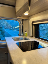 RV rental kitchen: modern sink, induction cooktop, and stunning mountain road views from a camper van window.