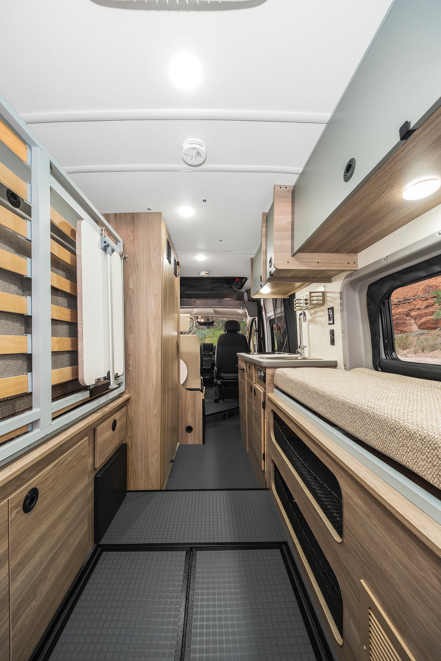 Spacious rv rental interior with bed, kitchen, storage, light wood cabinets, and grey floor.