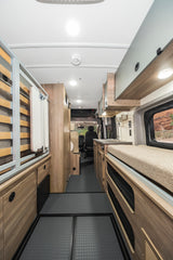 Spacious rv rental interior with bed, kitchen, storage, light wood cabinets, and grey floor.