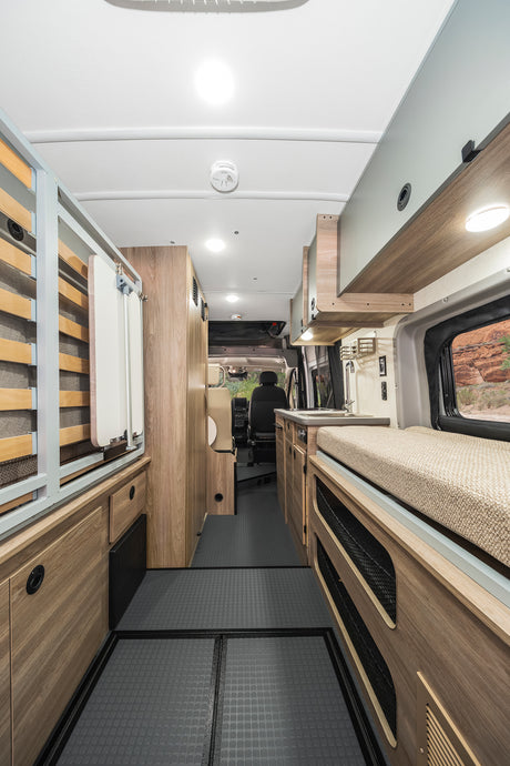 Spacious rv rental interior with bed, kitchen, storage, light wood cabinets, and grey floor.