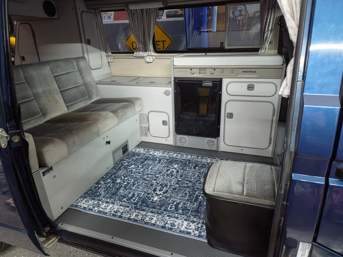  is nestled among trees and yellow flowers.|Explore this RV rental's cozy camper van interior. From the back — photo 3