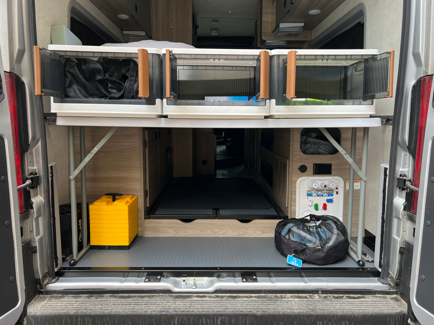 Organized RV rental rear storage with collapsible bins, water hookups, and leveling blocks.