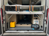 Organized RV rental rear storage with collapsible bins, water hookups, and leveling blocks.