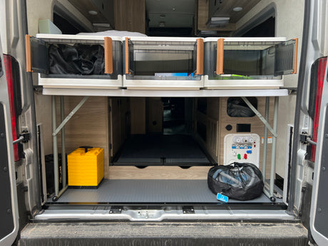 Organized RV rental rear storage with collapsible bins, water hookups, and leveling blocks.